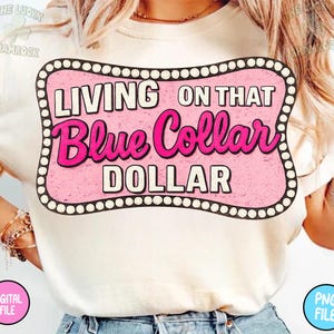 Puede incluir: Camiseta color crema con un gr&aacute;fico rosa y negro que dice "LIVING ON THAT Blue Collar DOLLAR". El gr&aacute;fico es de estilo retro, con un fondo rosa y texto blanco y rosa. La camiseta es un archivo digital.