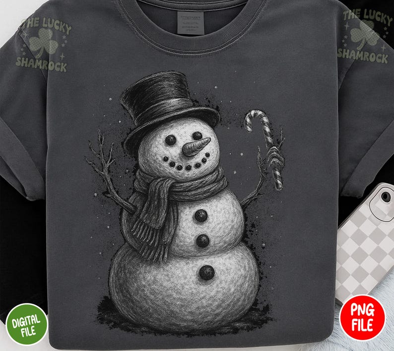 May include: Dark gray t-shirt featuring a detailed illustration of a snowman wearing a top hat and scarf, holding a candy cane. The snowman has a carrot nose and button eyes. The text "THE LUCKY SHAMROCK" is printed on the top left and right.