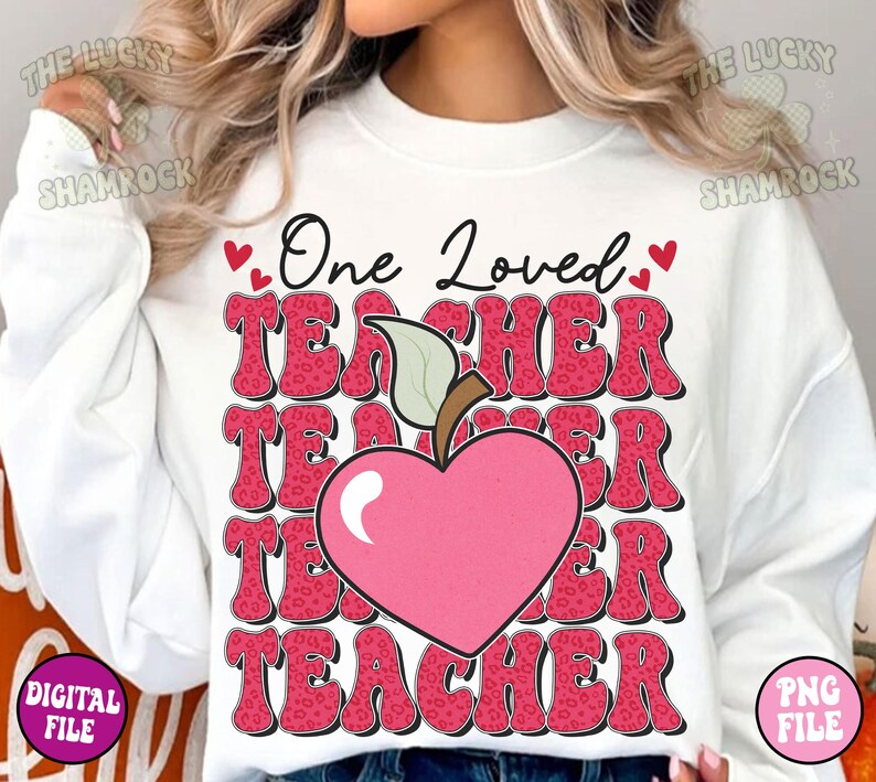 May include: White sweatshirt with a pink and red graphic design that says "One Loved Teacher" with a pink heart and apple design.