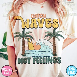 May include: A white t-shirt with a graphic design of a surfboard, palm trees, and a wave. The text "Catch Waves Not Feelings" is printed in green and yellow letters.