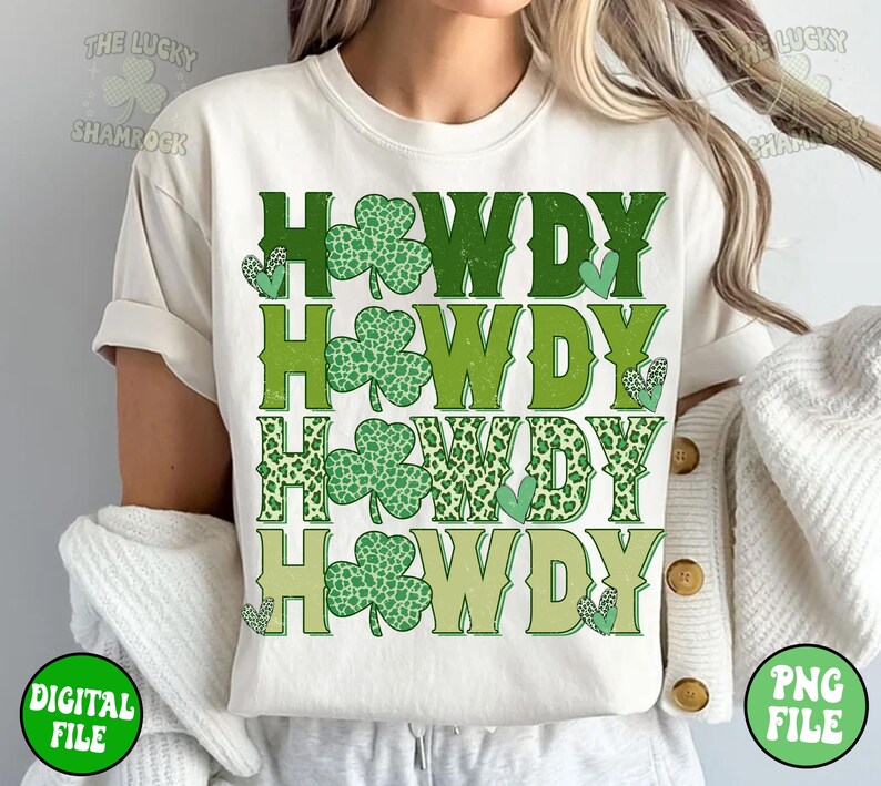 May include: A white t-shirt with the word "HOWDY" repeated four times in green, yellow, and brown. Each "HOWDY" is decorated with shamrock-shaped leaves. The shirt is being worn by a person.