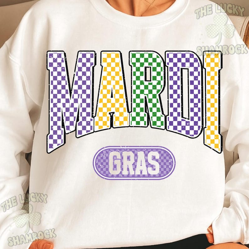 May include: White sweatshirt featuring the words "MARDI GRAS" in large, colourful, checkered letters. The word "MARDI" is in purple, yellow, and green. The word "GRAS" is in a purple oval. The sweatshirt has a vintage, distressed appearance.