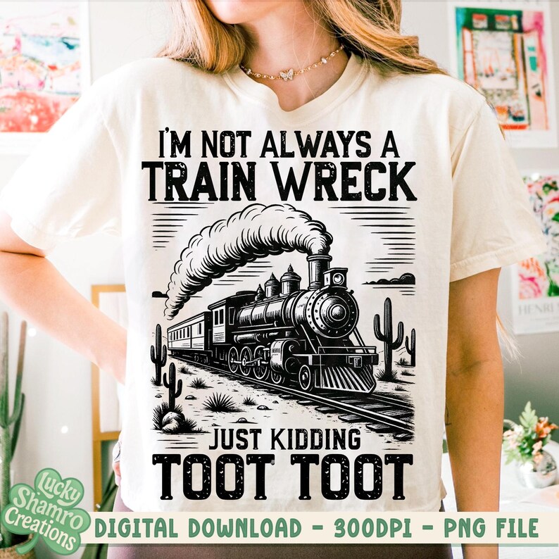 K&ouml;nnte beinhalten: Cremefarbenes T-Shirt mit einem schwarz-wei&szlig;en Zug-Grafik. Der Text lautet "I'M NOT ALWAYS A TRAIN WRECK JUST KIDDING TOOT TOOT." Das Design zeigt eine detaillierte Illustration eines Dampfzuges, Kakteen und Bahngleise.