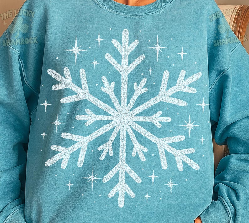 May include: A light blue sweatshirt featuring a large white snowflake design in the center, surrounded by smaller star shapes. The text "THE LUCKY SHAMROCK" is visible on the upper left side of the sweatshirt.