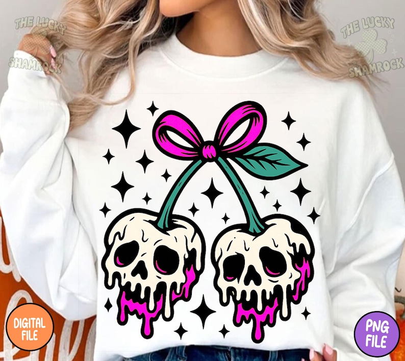 May include: White sweatshirt featuring a graphic of two cherries with skull faces, dripping with pink liquid. The cherries are connected by green stems and a pink bow. Black star shapes surround the cherries.