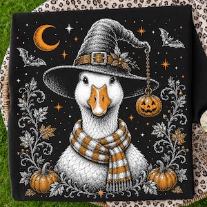 May include: A black fabric square featuring a detailed illustration of a white goose wearing a witch hat and a striped orange and white scarf. The design includes orange pumpkins, bats, a crescent moon, and stars, with a small pumpkin lantern hanging.