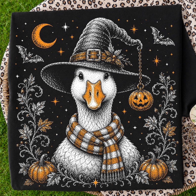 May include: A black fabric square featuring a detailed illustration of a white goose wearing a witch hat and a striped orange and white scarf. The design includes orange pumpkins, bats, a crescent moon, and stars, with a small pumpkin lantern hanging.