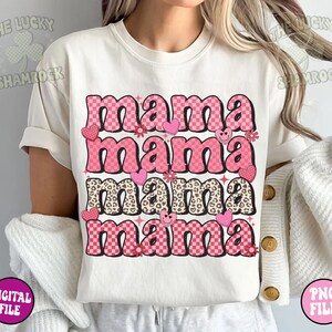 May include: A white t-shirt with the text "mama mama mama mama" in pink and black letters with different patterns. The letters are in a retro style with hearts, flowers, and smiley faces.