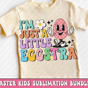 Puede incluir: Una camiseta amarillo claro con el texto "I'M JUST A LITTLE EGGSTRA" en letras de colores. El gr&aacute;fico incluye un personaje de huevo sonriente y a cuadros haciendo el signo de la paz. Tambi&eacute;n se muestra una margarita y una pi&ntilde;a.
