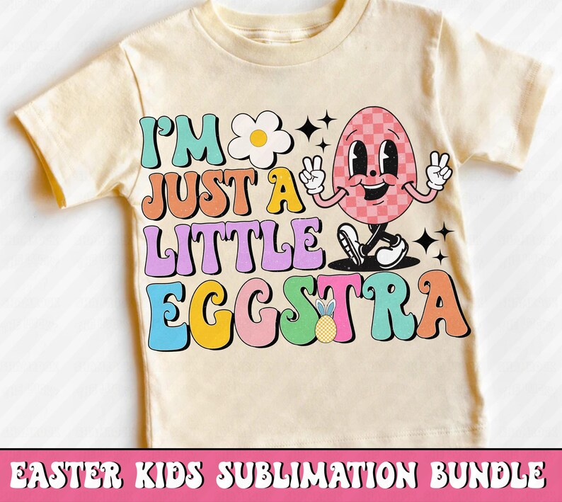 Puede incluir: Una camiseta amarillo claro con el texto "I'M JUST A LITTLE EGGSTRA" en letras de colores. El gr&aacute;fico incluye un personaje de huevo sonriente y a cuadros haciendo el signo de la paz. Tambi&eacute;n se muestra una margarita y una pi&ntilde;a.