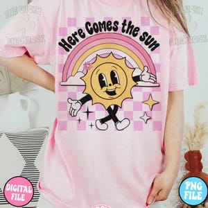 May include: Pink t-shirt with a graphic of a smiling sun with a rainbow and the text "Here Comes the Sun".