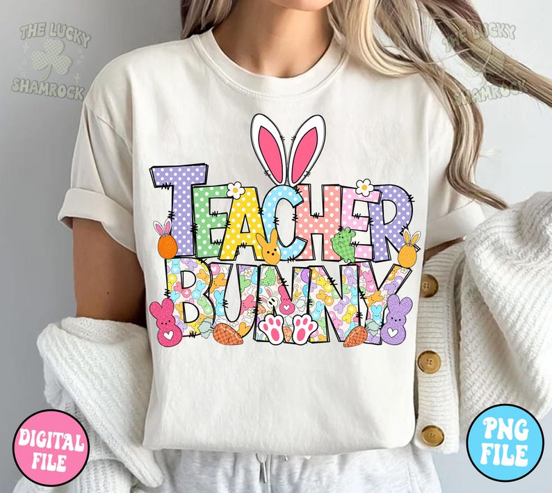 以下が含まれることがあります： 「Teacher Bunny」と書いてあるカラフルなグラフィックデザインが施された白いTシャツ。グラフィックには、ピンクの耳をしたウサギ、イースターエッグ、その他のイースターをテーマにした要素が描かれています。