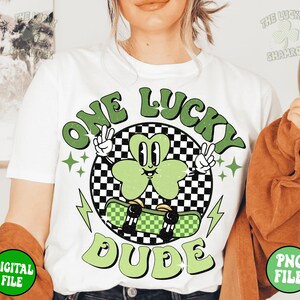 May include: White t-shirt with a green shamrock graphic and the text "One Lucky Dude" in a retro style.