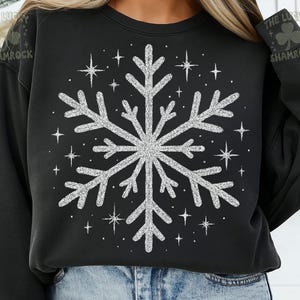 May include: Black sweatshirt featuring a large, sparkly silver snowflake design. Surrounding the snowflake are smaller starbursts. The text "THE LUCKY SHAMROCK" is printed on the upper right sleeve.