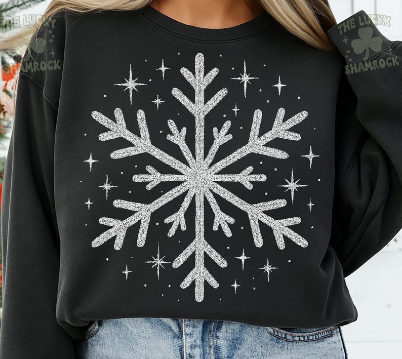 May include: Black sweatshirt featuring a large, sparkly silver snowflake design. Surrounding the snowflake are smaller starbursts. The text "THE LUCKY SHAMROCK" is printed on the upper right sleeve.