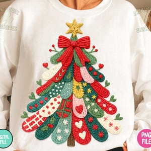 May include: White sweatshirt featuring a colorful, textured Christmas tree design. The tree is adorned with various patterns and embellishments, including a red bow, a gold star, and decorative elements. The design is made of various colors, including red, green, and yellow.