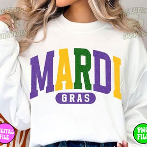 Puede incluir: Sudadera blanca con un gr&aacute;fico morado, verde y amarillo que dice "Mardi Gras".