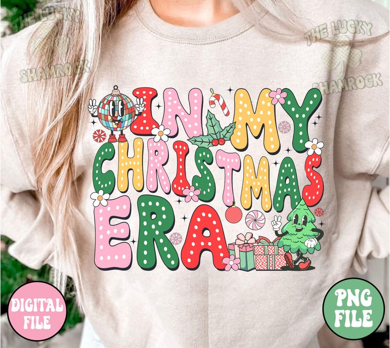 May include: Beige sweatshirt with the phrase "IN MY CHRISTMAS ERA" in colorful, retro-style lettering. The design includes a disco ball, candy cane, holly, and a cartoon Christmas tree. The words are outlined in various colors.
