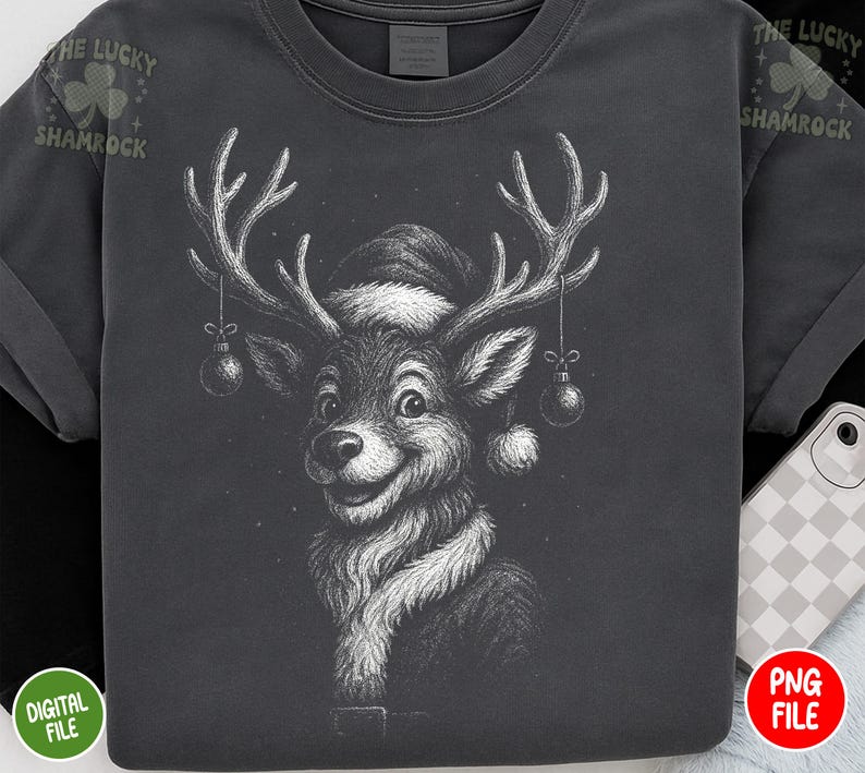 May include: Dark gray t-shirt featuring a detailed black and white illustration of a reindeer wearing a Santa hat and scarf. The reindeer has large antlers with ornaments hanging from them. The text "THE LUCKY SHAMROCK" is printed on the upper left sleeve.