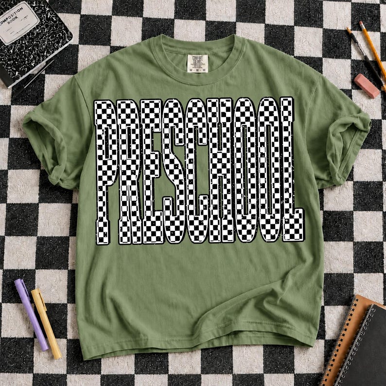 K&ouml;nnte beinhalten: Ein olivgr&uuml;nes Kurzarm-T-Shirt mit dem Wort "PRESCHOOL", das in einem auff&auml;lligen schwarz-wei&szlig;en Schachbrettmuster gedruckt ist. Die Buchstaben haben ein abgenutztes, strukturiertes Aussehen. Das T-Shirt hat einen Rundhalsausschnitt.