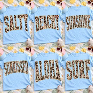 May include: Six light blue t-shirts with leopard print text that reads "SALTY", "BEACHY", "SUNSHINE", "SUNKISSED", "ALOHA", and "SURF". Each shirt has a crew neck and short sleeves. Sunglasses, hats, and shoes are also visible.