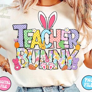 以下が含まれることがあります： 「Teacher Bunny」と書いてあるカラフルなグラフィックがプリントされた白いTシャツ。グラフィックには、ピンクの耳をしたウサギ、パステルカラーのドット、イースターをテーマにした様々な要素が描かれています。