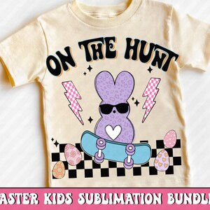 Puede incluir: Camiseta color crema con un conejito morado con gafas de sol en monopat&iacute;n. La camiseta tiene el texto "ON THE HUNT" e incluye rayos y huevos de Pascua. El dise&ntilde;o est&aacute; sobre un patr&oacute;n de tablero de ajedrez en blanco y negro.