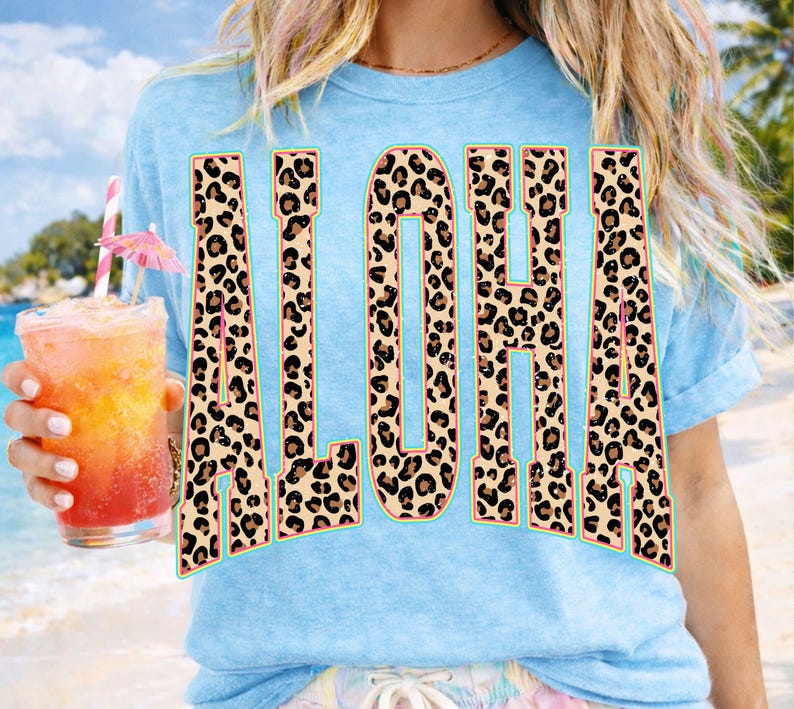 May include: Light blue t-shirt with the word "ALOHA" in large, leopard print letters. The letters have a teal outline. A tropical drink with a pink umbrella is held in the left hand.
