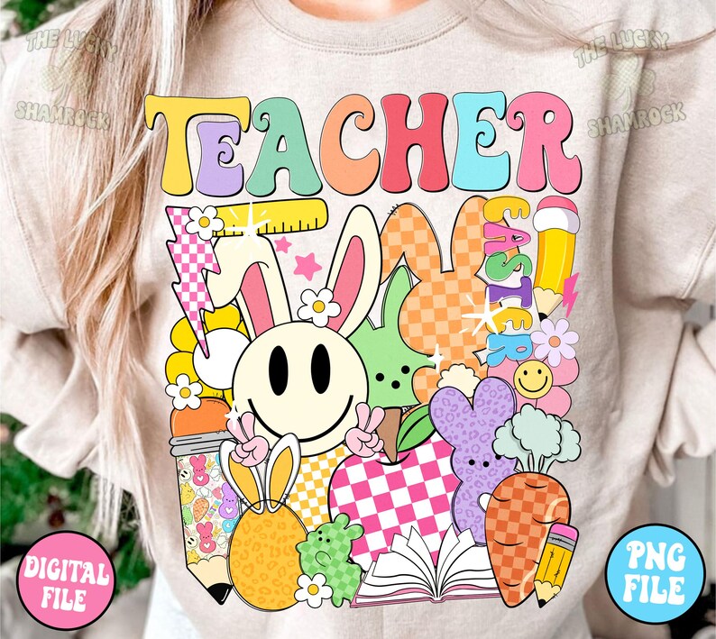 以下が含まれることがあります： 薄いベージュのTシャツに、カラフルなレトロな文字で「TEACHER」と書かれています。デザインには、笑顔のウサギ、チェック柄のリンゴ、本、その他カラフルな漫画の要素が描かれています。