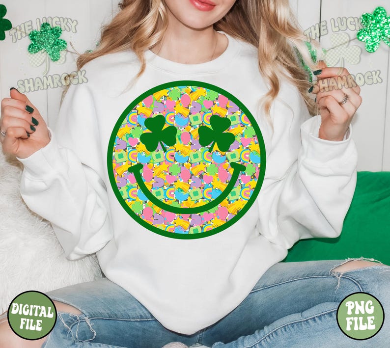 Peut inclure: Sweat-shirt blanc avec un motif de visage souriant vert. Le visage souriant est rempli de tr&egrave;fles, d'arcs-en-ciel et de pi&egrave;ces d'or color&eacute;s. Le texte "The Lucky Shamrock" est visible dans les coins sup&eacute;rieurs de l'image.