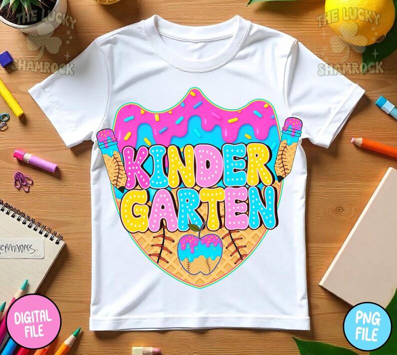 May include: White t-shirt with a colorful "Kindergarten" graphic. The design features a donut, ice cream cones, and an apple, all in vibrant pink, blue, and yellow hues. The shirt is a playful design for young children.