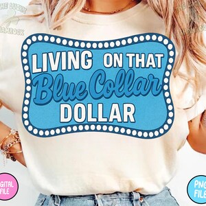 Puede incluir: Camiseta color crema con un dise&ntilde;o gr&aacute;fico azul y blanco que dice "LIVING ON THAT Blue Collar DOLLAR". El dise&ntilde;o gr&aacute;fico tiene un fondo azul claro y un borde blanco. La camiseta es un archivo digital.