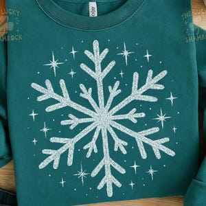 May include: Teal-colored sweatshirt featuring a large, white snowflake design in the center, surrounded by smaller starbursts. The text "THE LUCKY SHAMROCK" is visible in the upper left corner. The sweatshirt has a crew neck and long sleeves.