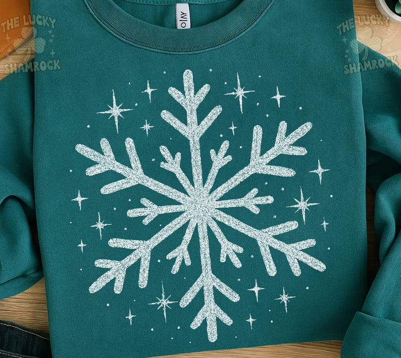 May include: Teal-colored sweatshirt featuring a large, white snowflake design in the center, surrounded by smaller starbursts. The text "THE LUCKY SHAMROCK" is visible in the upper left corner. The sweatshirt has a crew neck and long sleeves.