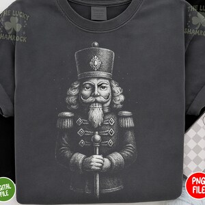 May include: Dark gray t-shirt featuring a detailed illustration of a nutcracker soldier. The design is in black and white, showcasing the soldier's uniform and facial features. The text "THE LUCKY SHAMROCK" is printed on the top left of the shirt.