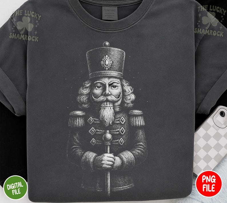 May include: Dark gray t-shirt featuring a detailed illustration of a nutcracker soldier. The design is in black and white, showcasing the soldier's uniform and facial features. The text "THE LUCKY SHAMROCK" is printed on the top left of the shirt.