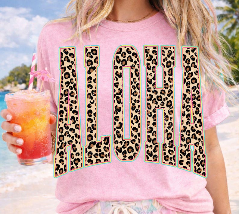 May include: Pink t-shirt with the word "ALOHA" in large, bold letters. The letters have a leopard print pattern with a teal outline. A tropical drink with a pink umbrella is held in the left hand.