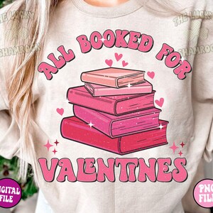 May include: A pink and white graphic design on a light beige t-shirt. The design features a stack of books with hearts and the text "All Booked For Valentines".