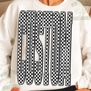 May include: A white long-sleeve sweatshirt featuring a large, bold graphic on the front. The graphic consists of the word CUSTOM written in tall, elongated letters filled with a black and white checkerboard pattern. The text is centered on the chest.