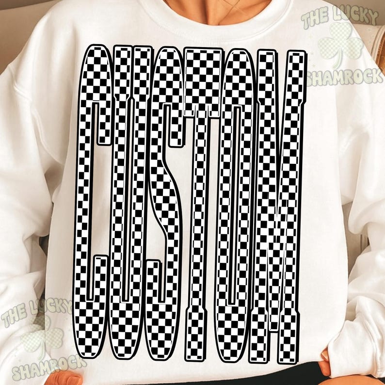 May include: A white long-sleeve sweatshirt featuring a large, bold graphic on the front. The graphic consists of the word CUSTOM written in tall, elongated letters filled with a black and white checkerboard pattern. The text is centered on the chest.