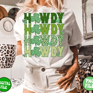 May include: White t-shirt with the text "Howdy" repeated four times in green, yellow, and leopard print. Each "Howdy" is decorated with a green shamrock.