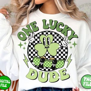 May include: White sweatshirt with a green shamrock character skateboarding and the text "One Lucky Dude" in green letters.