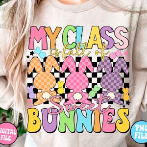 以下が含まれることがあります： レインボーカラーで「My Class is full of Sweet Bunnies」と書かれた薄いベージュの長袖シャツ。テキストは市松模様と、パステルカラーと市松模様のウサギの画像で囲まれています。
