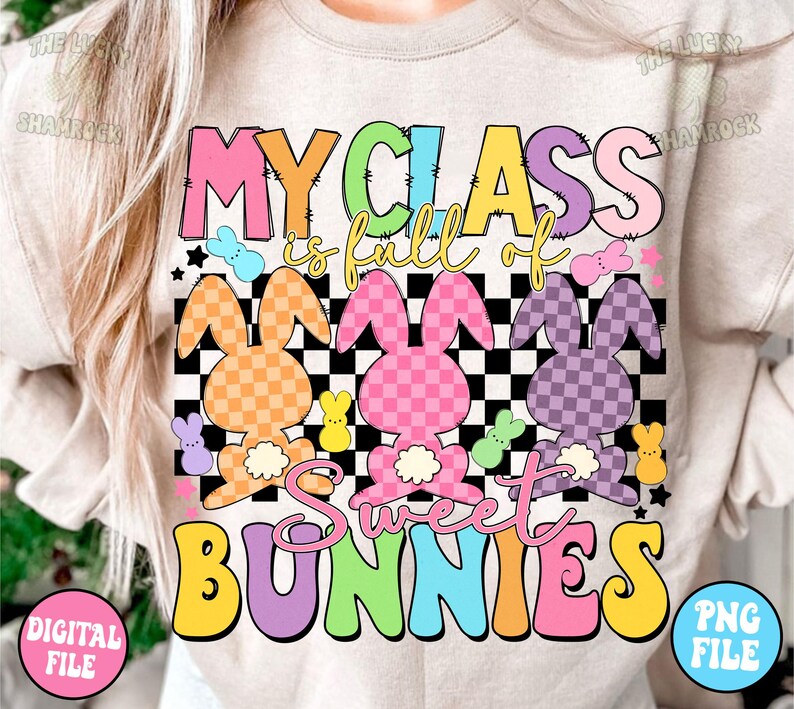 以下が含まれることがあります： レインボーカラーで「My Class is full of Sweet Bunnies」と書かれた薄いベージュの長袖シャツ。テキストは市松模様と、パステルカラーと市松模様のウサギの画像で囲まれています。