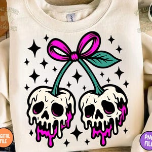 May include: Cream-colored sweatshirt featuring a graphic of two cherries with skull faces, dripping with pink liquid. The cherries are connected by a green stem and a pink bow. Black star shapes surround the cherries.