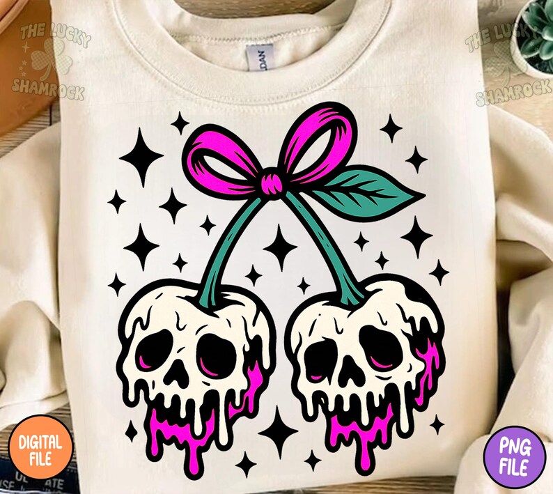 May include: Cream-colored sweatshirt featuring a graphic of two cherries with skull faces, dripping with pink liquid. The cherries are connected by a green stem and a pink bow. Black star shapes surround the cherries.