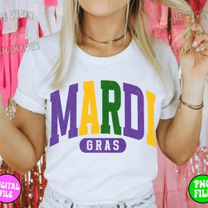 Puede incluir: Una camiseta blanca con un gr&aacute;fico morado, verde y amarillo que dice "Mardi Gras".