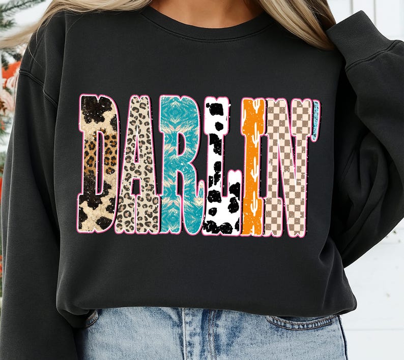 May include: Black crewneck sweatshirt with the word "DARLIN'" in a colorful, patterned design. The letters feature animal print, turquoise, cow print, orange cactus, and a checkered pattern, outlined in pink.