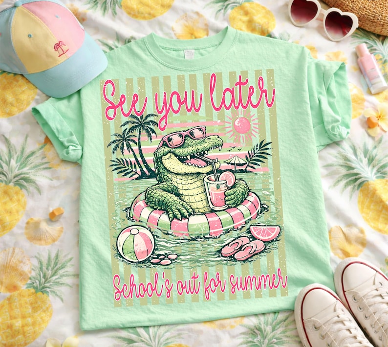 May include: A pale green t-shirt featuring a cartoon alligator in sunglasses, relaxing in a pool with a drink. The shirt has the phrases "See you later" and "School's out for summer" printed on it.