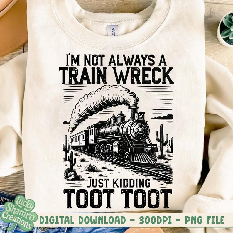 K&ouml;nnte beinhalten: Cremefarbenes Sweatshirt mit einer schwarz-wei&szlig;en Grafik einer alten Dampflokomotive. Der Text lautet "I'M NOT ALWAYS A TRAIN WRECK JUST KIDDING TOOT TOOT". Das Design beinhaltet Kakteen und Bahngleise.